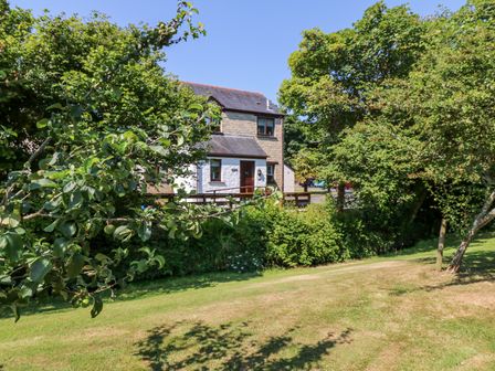 A stone and white house surrounded by trees and a grassy area at Tranquility in Falmouth