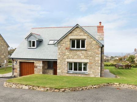 A stone house with a grey roof and grass lawn in front and wooden outdoor furniture on the side at Myles View in Pendeen