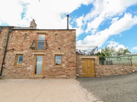 An exterior view of a stone house with wooden doors windows and a balcony with outdoor furniture at Apple Tree Cottage Bleatarn near Kirkby Stephen