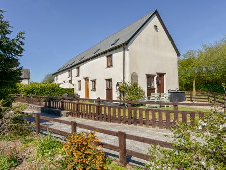 A white two-story house with brown doors and windows surrounded by a wooden fence and garden at Post House in Holsworthy