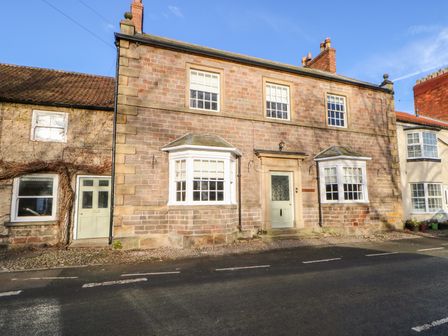 A stone brick house with white framed windows and a green door by the roadside at Stepping Stones in Catterick North Yorkshire