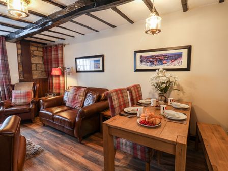 A living room with leather sofas plaid cushions a wooden dining table with place settings and flowers at Midships Cottage in Whitby