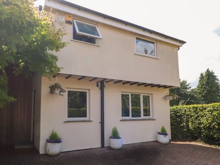 The exterior of a two story house with three windows and potted plants near the entrance at Palm Court in Burton-in-Kendal