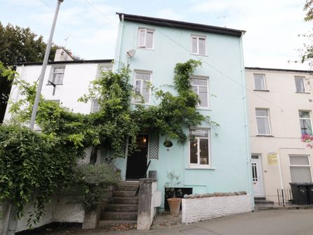 A three-story blue house with greenery over the entrance and a small stairway leading to a black front door at Waverley House in Beaumaris