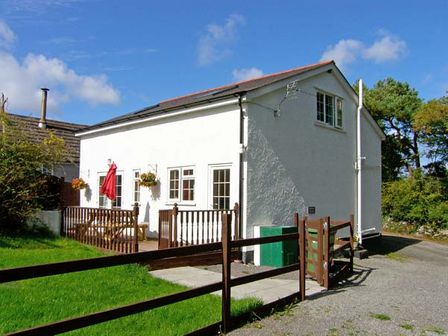 A white two-story cottage with brown wooden fencing and a red umbrella on the patio at Farmhouse Cottage in Pentraeth
