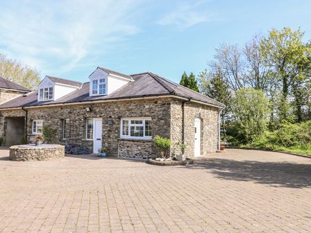 A stone house with a tiled roof and several windows surrounded by trees and a paved driveway at Fisher Granary in Lampeter