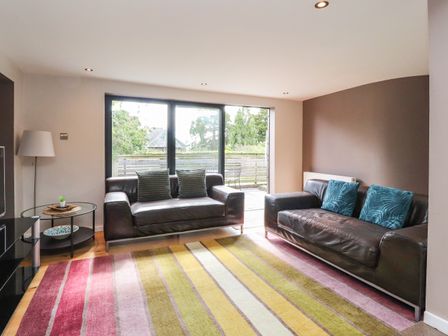 A living room with two leather sofas, cushions, a striped rug, glass door, and side table at Underfell in Burton-In-Kendal