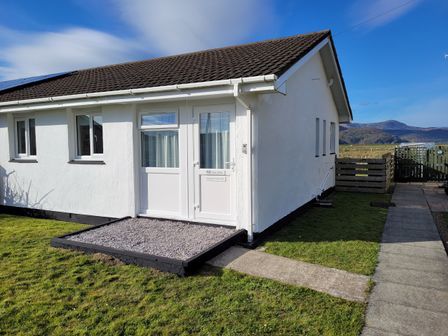 A white single-story house with a brown tiled roof and three windows at 48 Glan Y Mor in Fairbourne