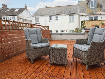 A wooden deck with two wicker chairs and a small wicker table at Flat 1 in Penzance