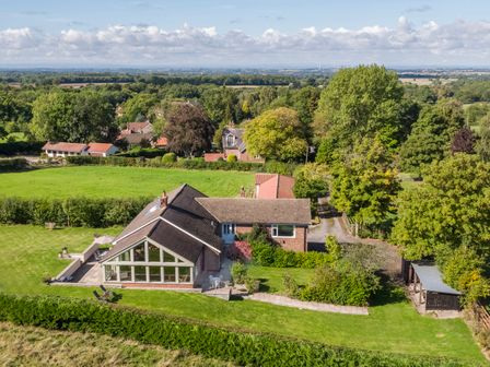 A house with a patio and garden surrounded by trees and fields at The Lodge in Ingleby Greenhow