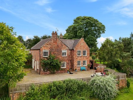 A brick house with multiple windows a blue bench and outdoor furniture in a fenced yard with trees at Manor Cottage in Northallerton