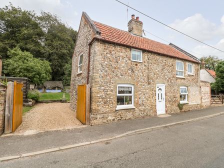 A stone house with orange roof tiles and white windows next to an open wooden gate and gravel driveway at Garden House in Northwold