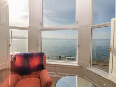 A room with a red armchair and a blanket near windows overlooking the sea at 11 Marine Terrace in Criccieth
