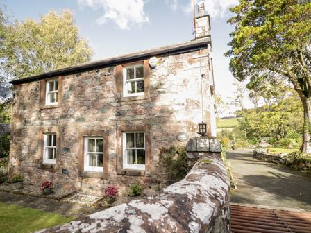 A stone house with white framed windows and a stone wall in front surrounded by trees and a driveway at Fell Foot in Santon Bridge near Eskdale Green