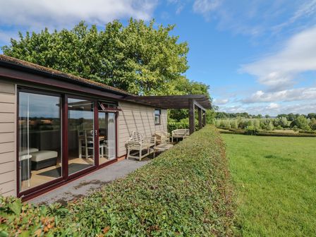 An outdoor patio area with wooden benches and tables next to a building with glass doors overlooking a grassy field at Upham View in Woodbury