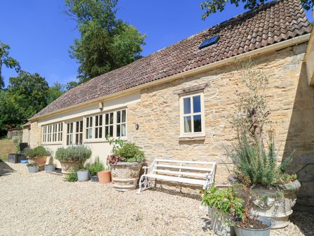 A stone building with windows and plant pots at Upper Mill Barn, Coln St Aldwyns, near Bibury