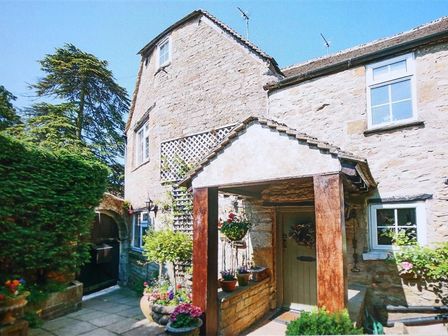 Stone exterior of a house with a small covered porch and potted plants near the door at Pike Cottage in Stow-On-The-Wold