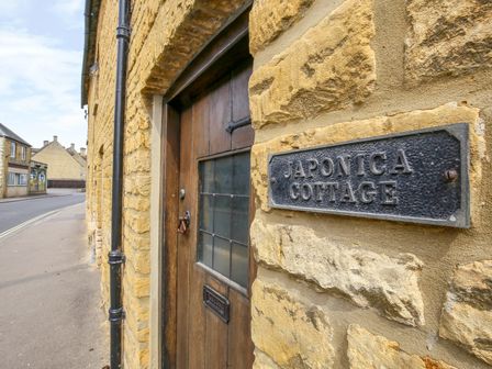 A close up of a wooden door with a sign reading Japonica Cottage on a stone wall at Japonica Cottage in Bourton on the Water