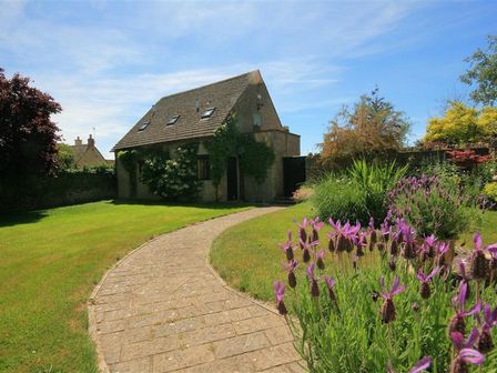 A stone house with a tiled roof a curved stone pathway and garden plants at Temple Mews in Broadwell near Stow-on-the-Wold