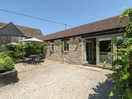 An outdoor patio area with a table and chairs under an umbrella next to a stone building at Saddlebacks Barn in Burford