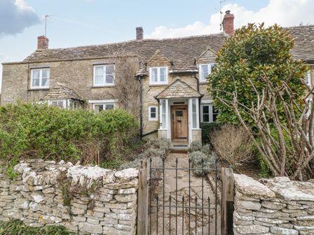 An old stone cottage with a wooden door behind a metal gate and stone wall at Brooklands in Chedworth