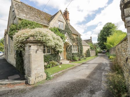 Stone house with ivy on the walls next to a narrow road with a car at The Lodge in Coln St Aldwyns
