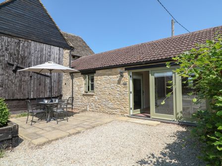 An outdoor patio with table chairs and umbrella next to a stone building with open glass doors at Ewecub Barn in Burford