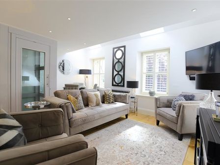 A living room with sofas armchairs a rug lamps and a wall-mounted television at The Hive in Stow-On-The-Wold