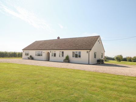 A single story house with multiple windows and a gravel driveway surrounded by grass at The Clealings in Witney