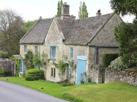 A stone house with blue trim on windows and doors surrounded by greenery and a stone wall at The Malt House in Windrush near Burford