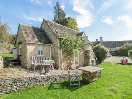 A stone cottage with outdoor wooden furniture on a grassy lawn at Mayfly Cottage in Coln St Aldwyns near Bibury