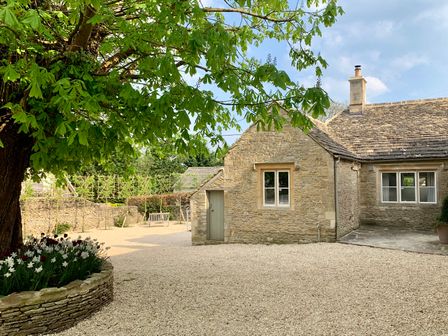 An outdoor area with a stone building gravel ground and a tree with flowers at The Old Dairy in Shilton