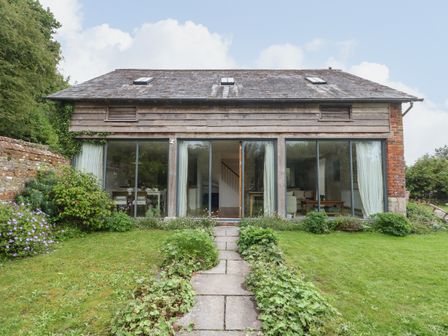 A house with large glass windows and a stone path leading to it surrounded by a garden at The Cart Barn in Ridge near Chilmark