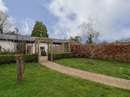 A garden with a gravel path and wooden archway leading to a building with white walls and wooden framed windows at Pippin in Martin
