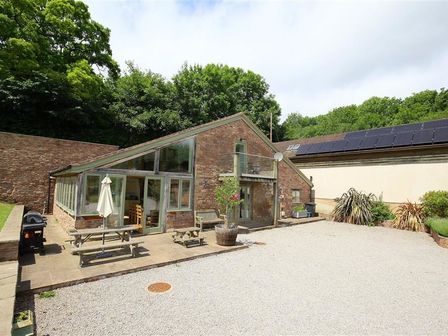 A brick house with glass windows patio table and umbrella gravel driveway and trees in background at The Old Mill in Flaxley