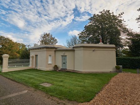 A single story cream colored building with a green door and surrounding grass and gravel at East Lodge in Rockbourne