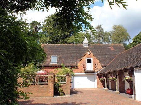 A courtyard with a brick driveway surrounded by brick buildings and hanging flower baskets at Granary Cottage in Royal Tunbridge Wells