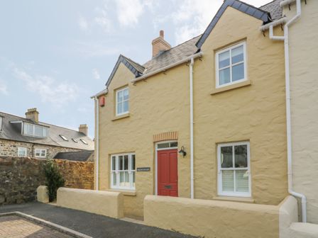 A cream-colored house with a red door and white-framed windows with a small wall in front at Craigluscar in Newport Pembrokeshire