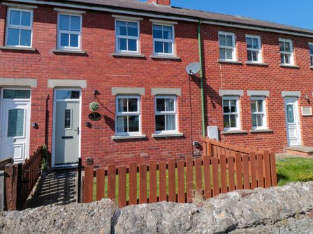 A row of brick townhouses with white framed windows and doors and a wooden fence in front at The Tannery in Whitby