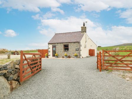 A sealed courtyard with gravel driveway leading to a small stone cottage with wooden gates at Ty Bach Ysgo in Aberdaron