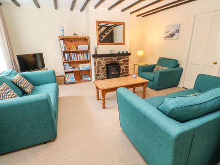 A living room with teal sofas a wooden coffee table a bookshelf a stone fireplace and a television at The Chace in Portreath