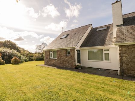 A stone and white house with a grey tiled roof and a green lawn at Llain Bach in Llangefni