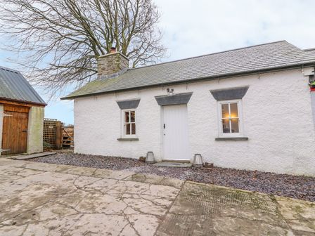A white cottage with two windows and a door situated on a paved area at Bwthyn Lan in Boncath