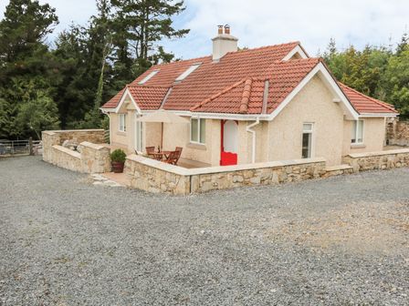 A single-story house with a red tiled roof and stone wall surrounding a patio with a table and umbrella at Cnoc suan in Aughavas County Leitrim