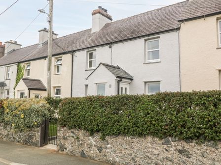 A row of attached stone houses with a hedge and stone wall in front at 3 Green Terrace in Llangaffo near Newborough