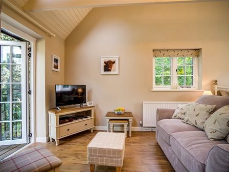A living room with a sofa, TV on a stand, small tables, and a door opening to the outside at Lime Tree in Burford