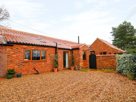 A gravel courtyard with potted plants and brick buildings with tiled roofs at Honey Buzzard Barn in Fakenham