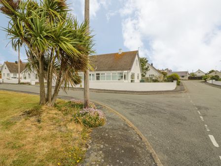 A street corner with a small tree flowers and matching white houses at Ty Taid in Rhosneigr