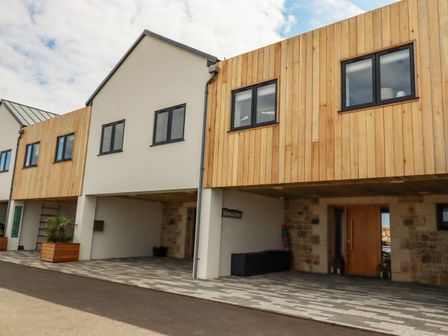 A modern building exterior with wood paneling and stone walls featuring windows and a wooden door at Stargazers in Sennen