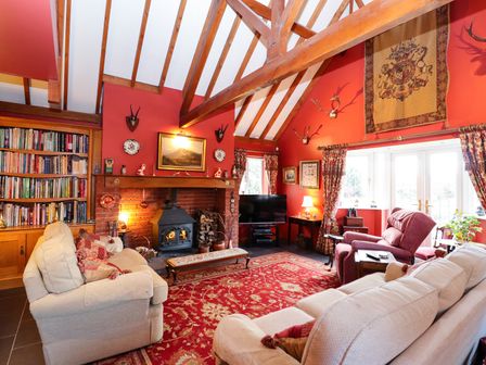 A living room with wooden beams a fireplace bookshelves sofas and red patterned carpet at The West Wing in Bodfari